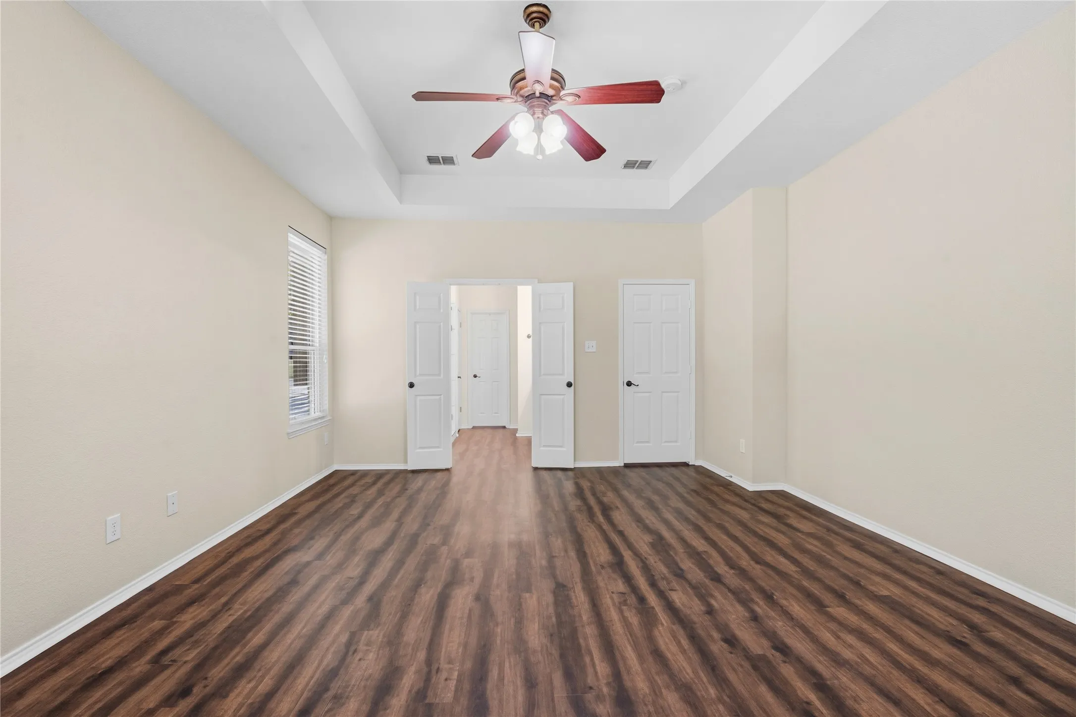 Spacious room featuring wood-finish flooring, a tray ceiling, and a ceiling fan with integrated lighting