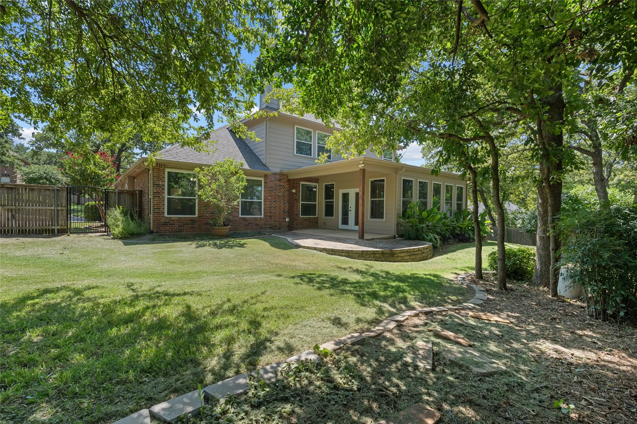 Expansive backyard featuring a brick and siding exterior, a covered patio with a built-in planter, large windows, and mature trees providing natural shading