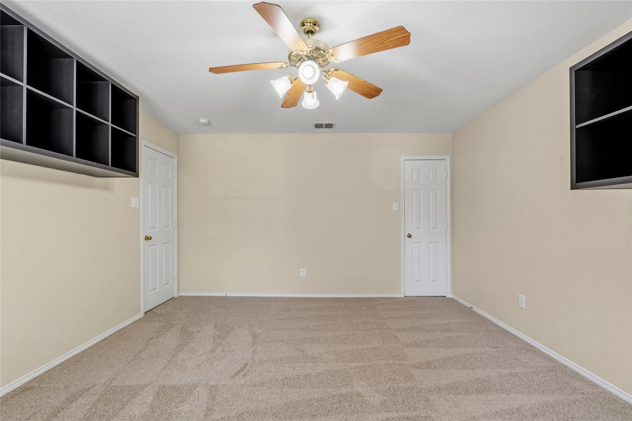 Spacious room featuring neutral carpeting, light-colored walls, and a ceiling fan with integrated lighting