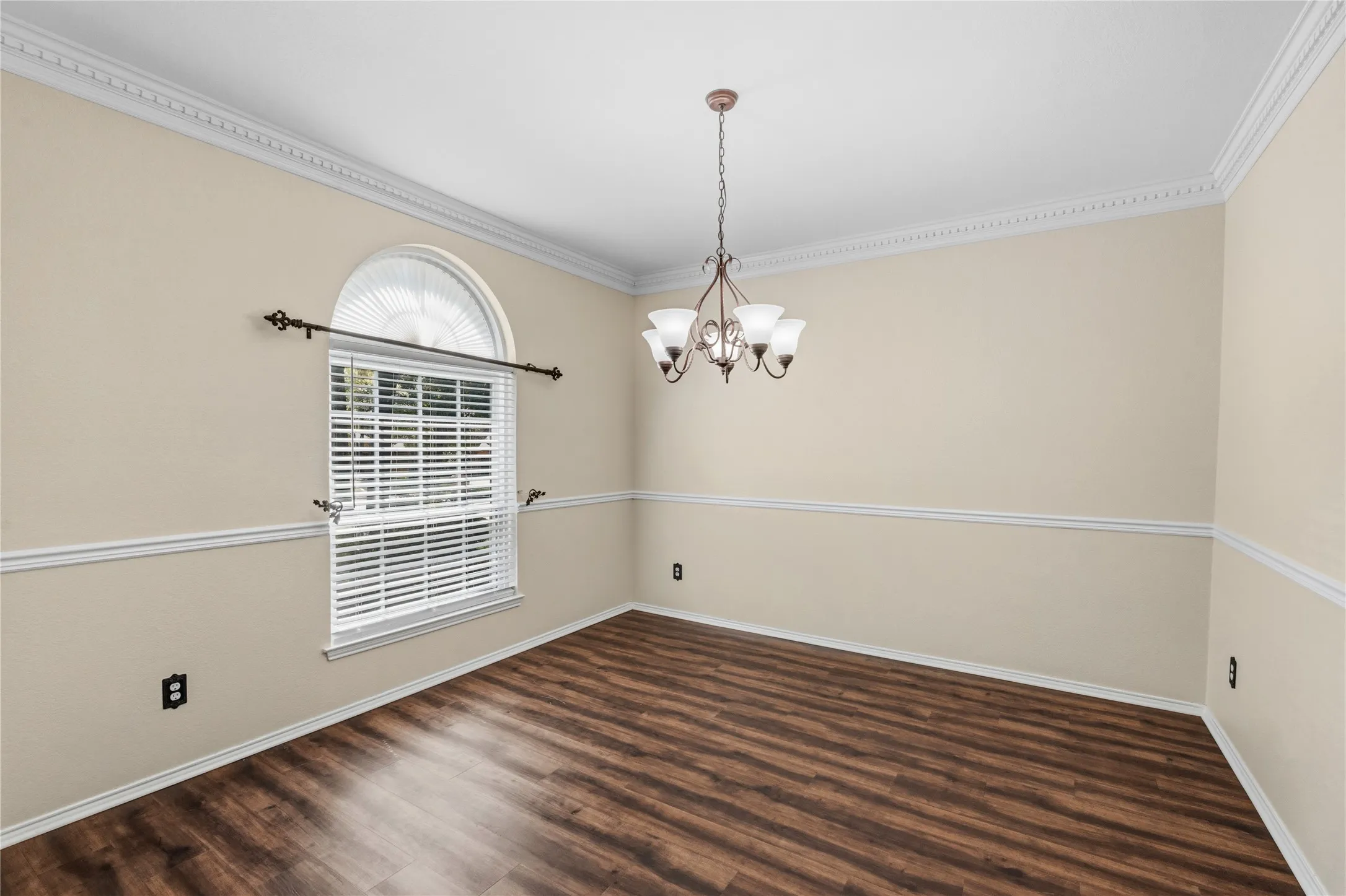 Room featuring wood-finish flooring, a tiered chandelier, and a window with an arched transom