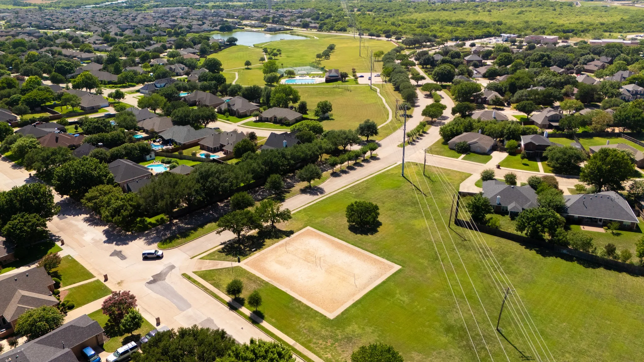 Expansive neighborhood showcasing mature trees, multiple properties with private swimming pools, and a nearby community park with a sand volleyball court and walking paths