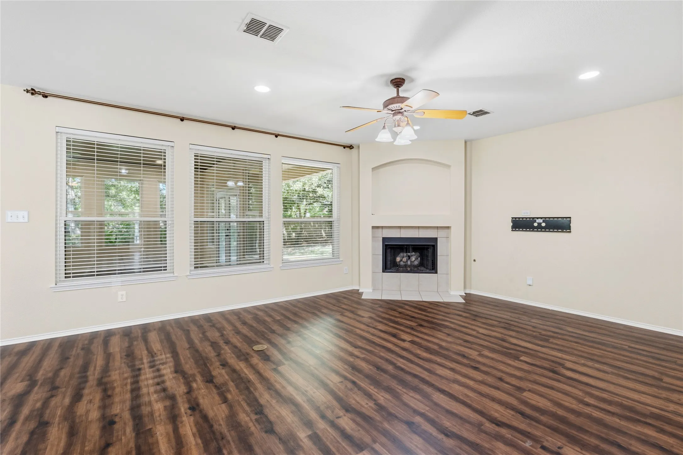 Spacious room featuring wood-finish flooring, a tile-surround fireplace with an arched alcove, and multiple windows providing natural illumination