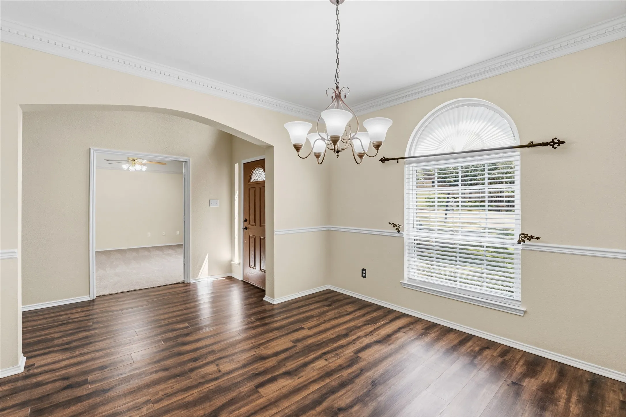 Spacious room featuring rich wood-finish flooring, an arched entryway, and a decorative chandelier