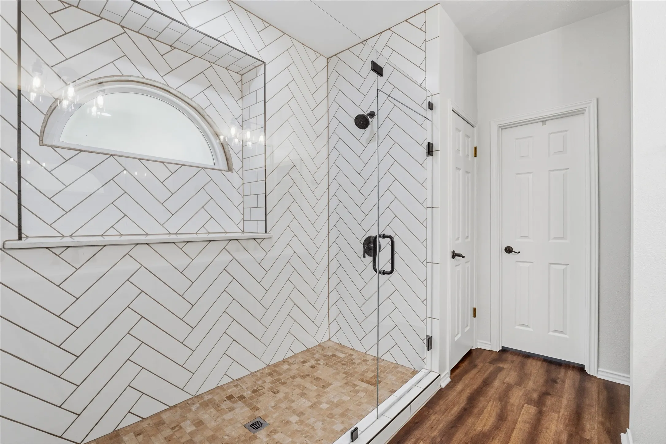 Enclosed glass shower featuring white subway tile in a herringbone pattern and a semicircular transom window