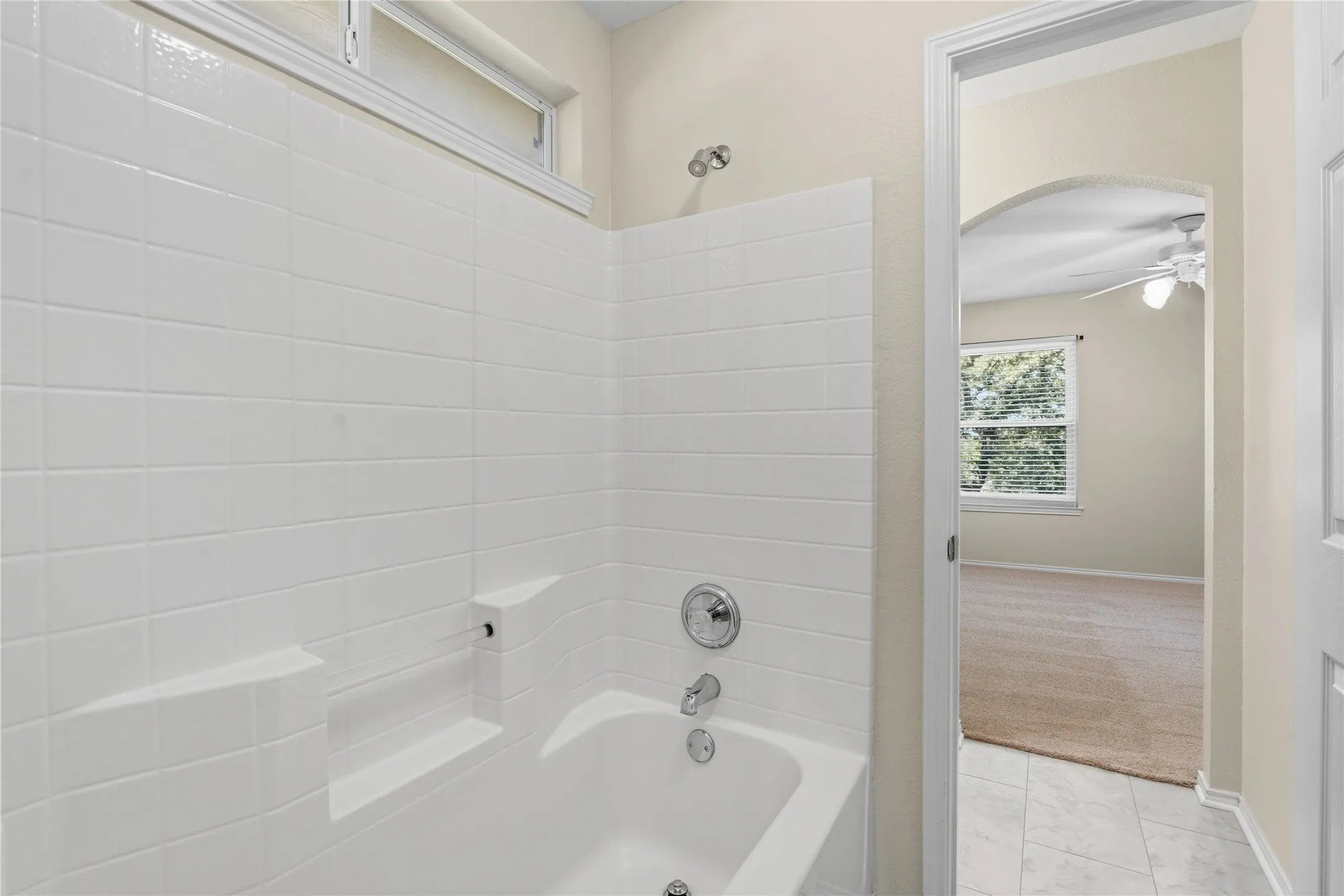 White subway tile surround with integrated soap dish and shelf, polished chrome bath fixtures, and an opaque transom window