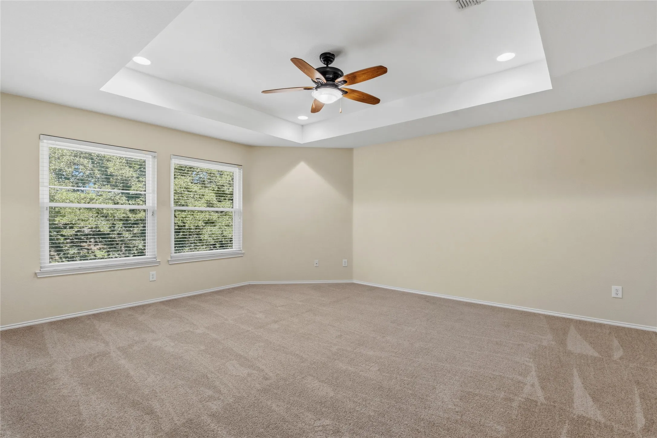 Spacious room featuring a tray ceiling with recessed lighting and a ceiling fan