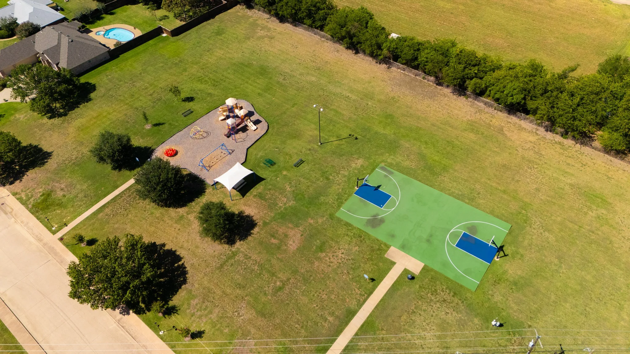 Expansive green space featuring a playground, basketball court, paved pathways, and mature trees