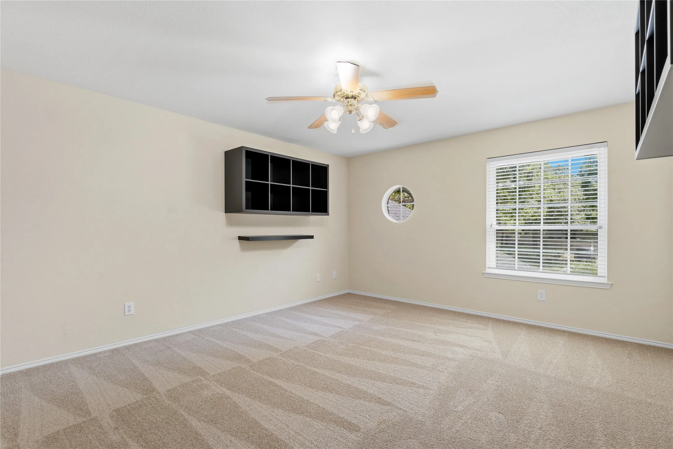 Bright room featuring a large rectangular window with horizontal blinds, a circular accent window, and patterned carpeting