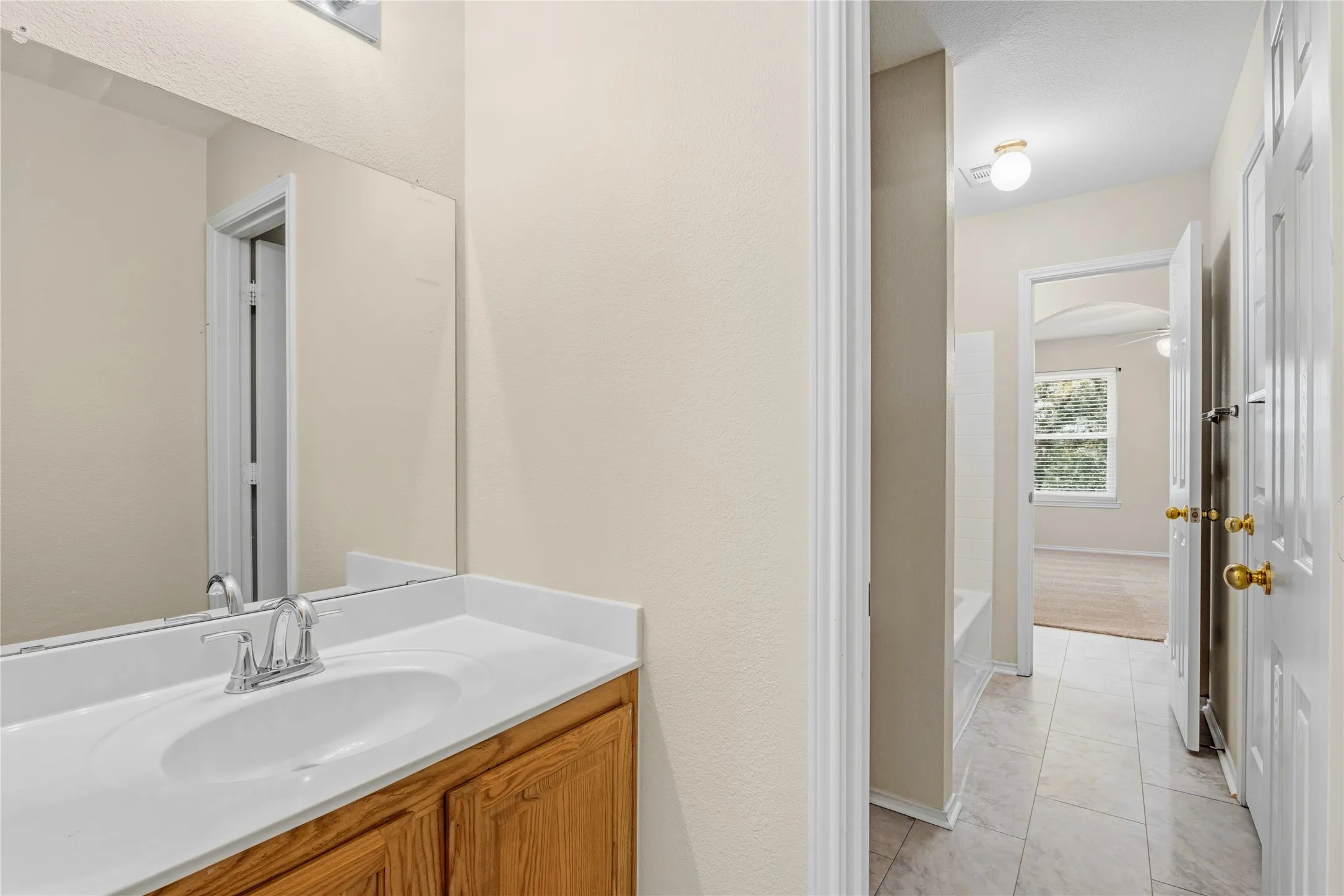 Bathroom vanity with a white countertop and integrated sink, complemented by a chrome faucet and wood-finish cabinetry