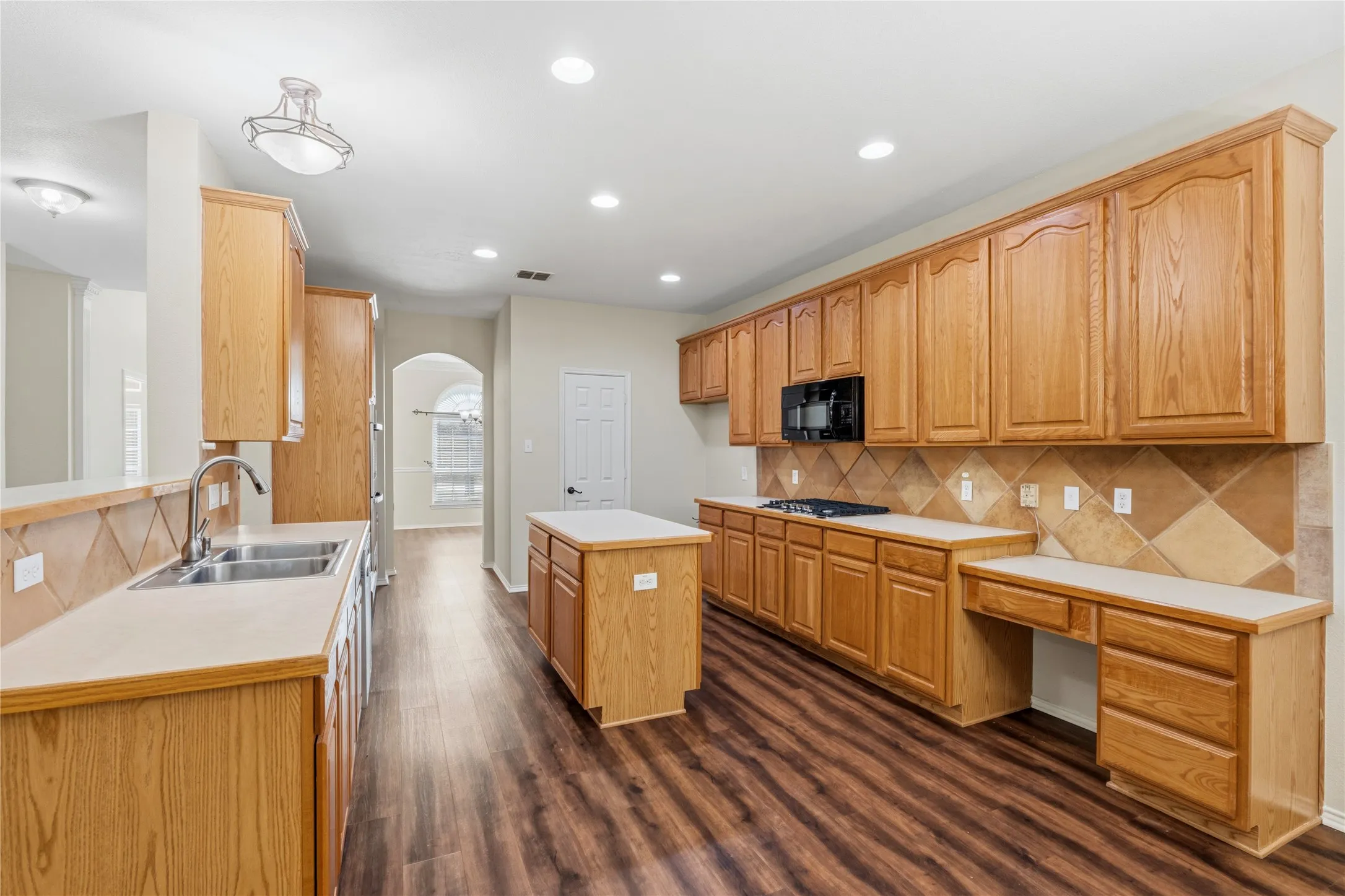 Kitchen featuring wood-finish cabinetry, a central island, wood-finish flooring, a tile backsplash, and recessed lighting