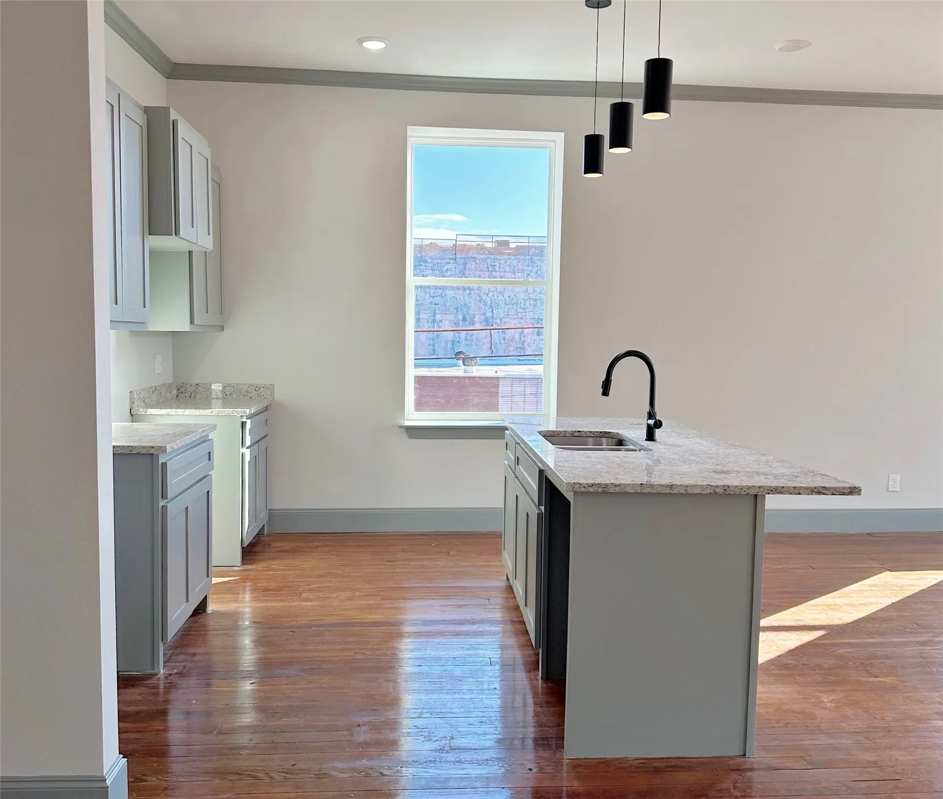 Kitchen island featuring a stainless steel sink with a matte black faucet, granite-style countertop, and gray shaker-style cabinetry