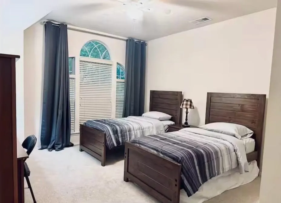 Bedroom featuring arched windows with blinds, light-toned carpeting, and a ceiling fan