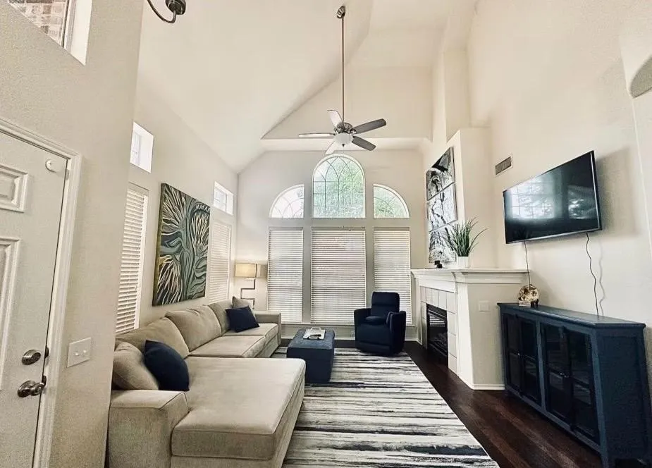 Living area featuring a vaulted ceiling with a fan, arched windows, transom windows, a fireplace with a tiled surround, and wood-finish flooring