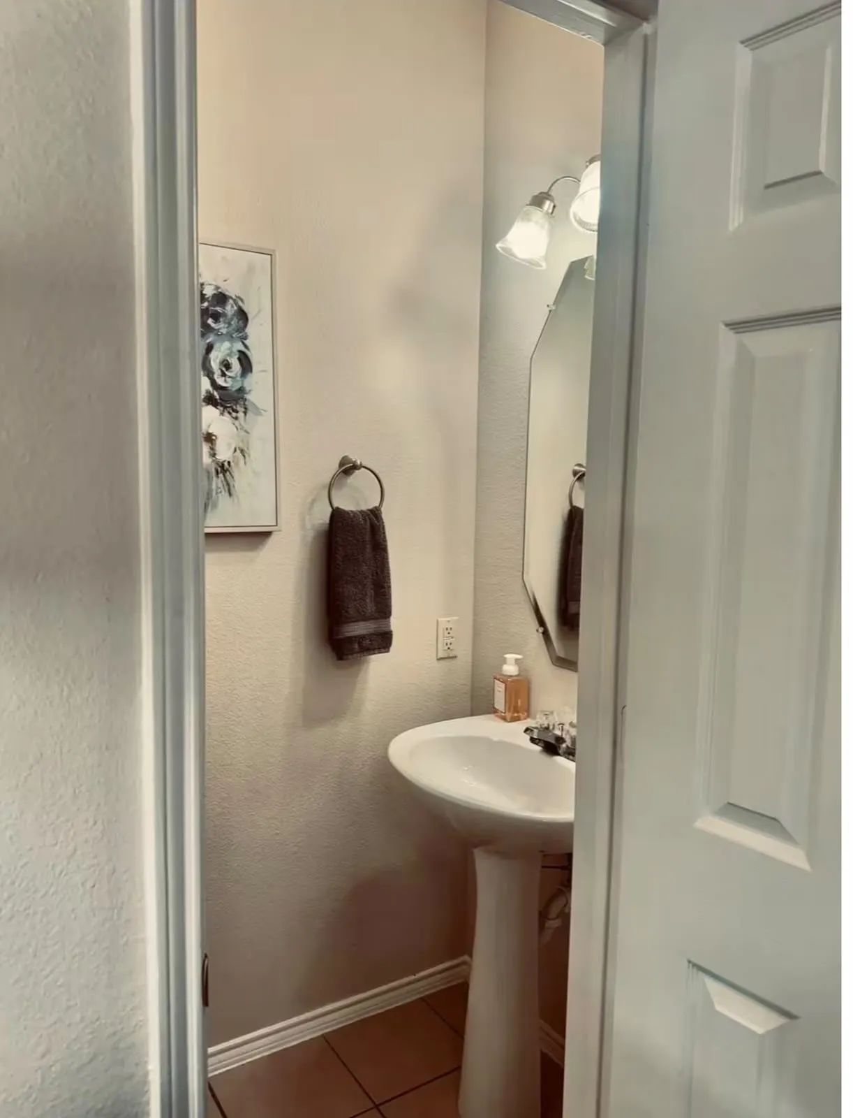 Pedestal sink with chrome faucet, octagonal mirror, and a two-bulb vanity light fixture