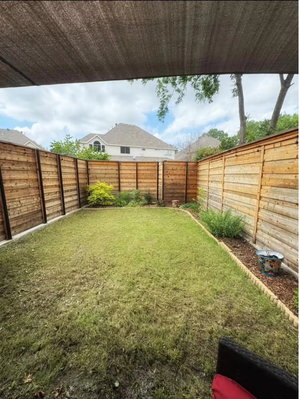 Fenced backyard featuring a lawn area, planting beds with mulch, and a privacy fence