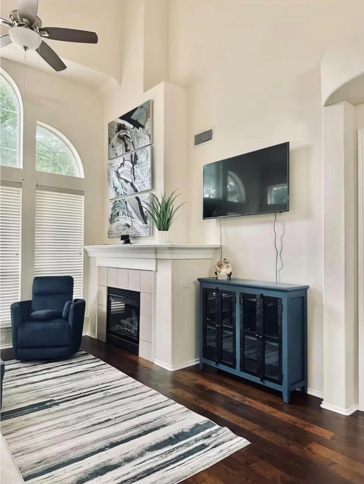 Two-story living area featuring a fireplace with a tiled surround, high vaulted ceilings, wood-finish flooring, and arched windows
