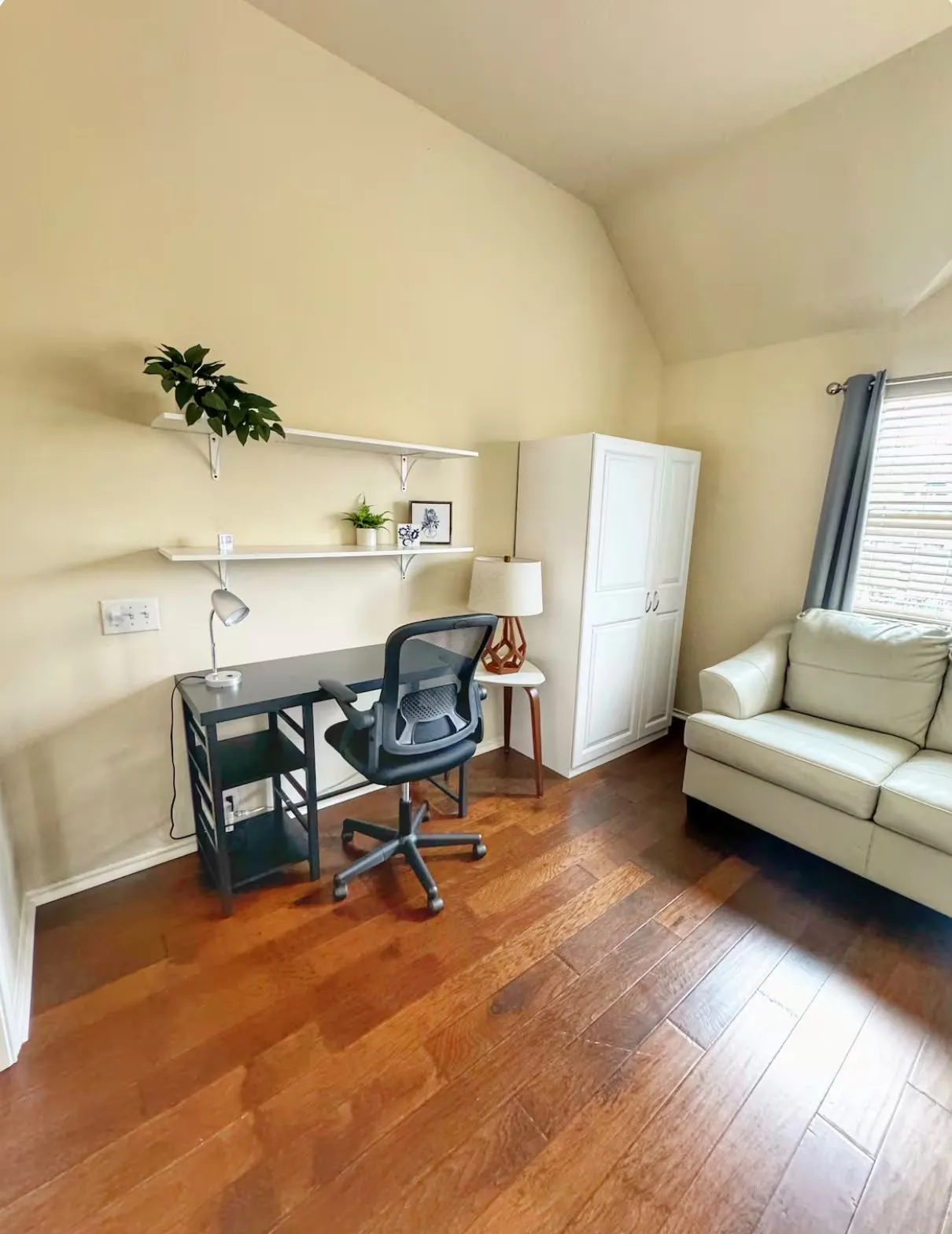 Wood-finish flooring throughout, featuring a built-in white cabinet, light beige wall color, and white wall shelving