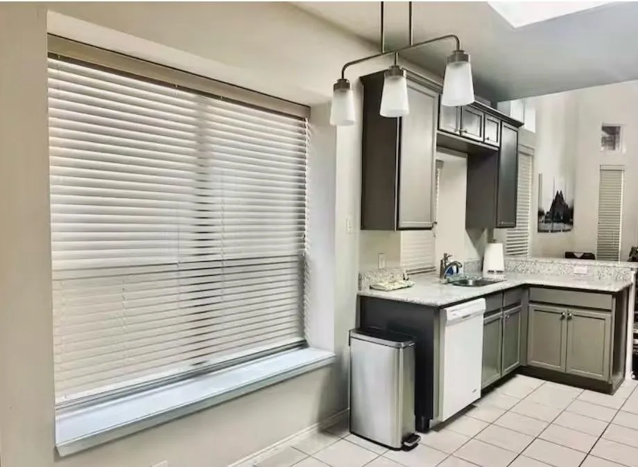 Kitchen featuring L-shaped cabinetry with a white dishwasher, stainless steel sink, and light granite-style countertops