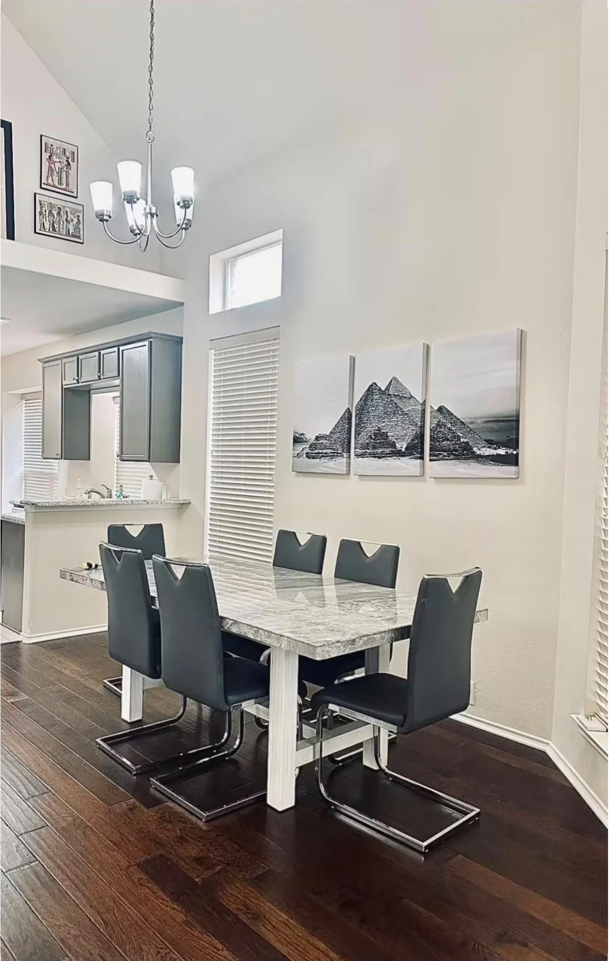 Vaulted ceilings with a contemporary chandelier, hardwood-finish flooring, and a kitchen pass-through with grey cabinetry