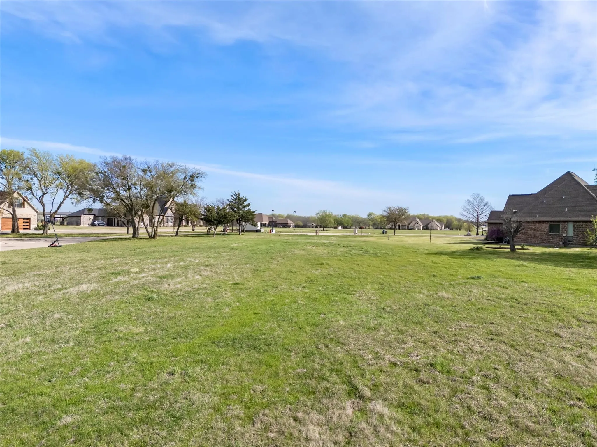 Expansive green space featuring scattered mature trees and distant residential structures