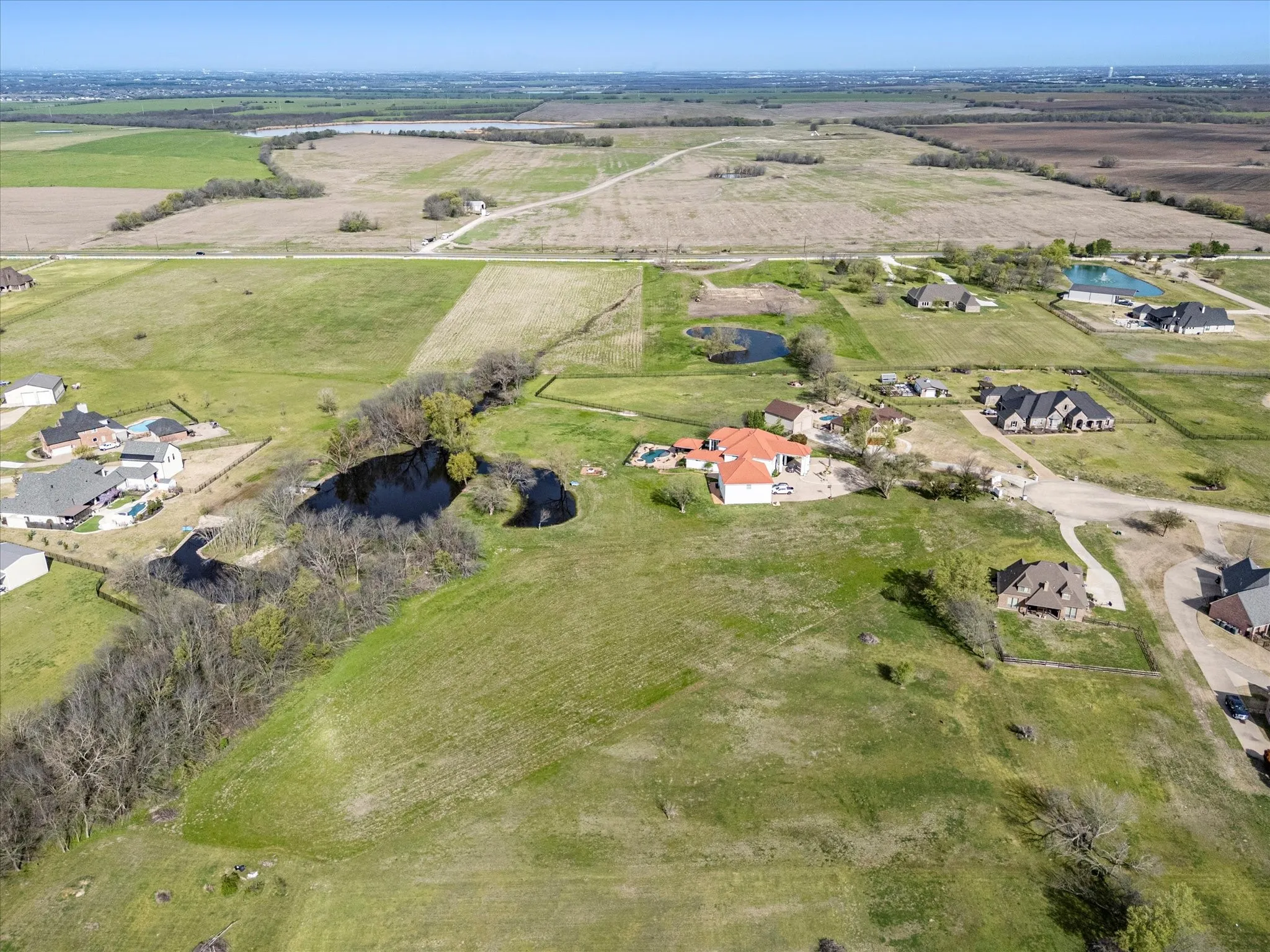 Expansive rural landscape featuring a custom home with a red tile roof, an integrated swimming pool, and a paved patio area