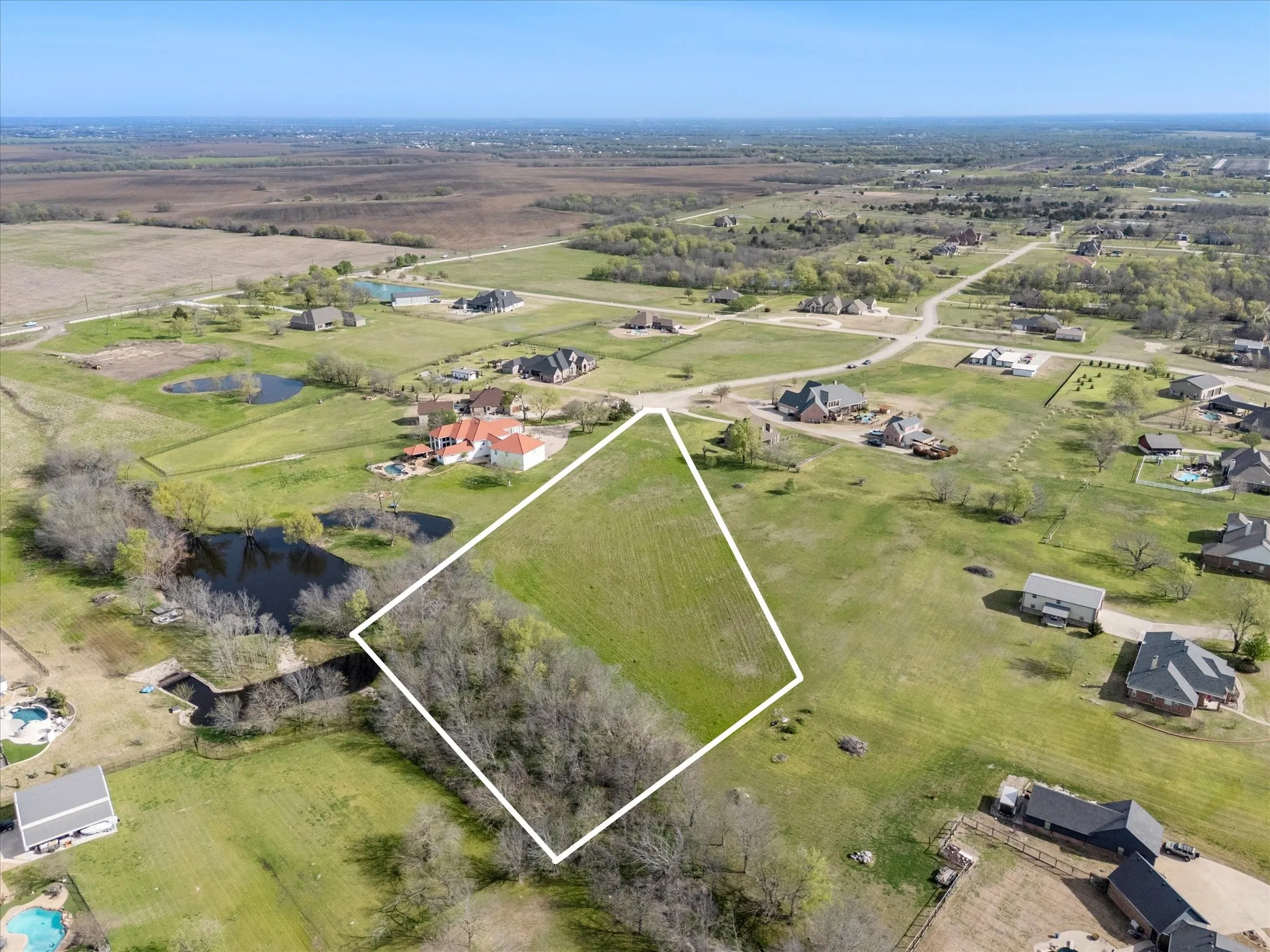 Expansive land parcel featuring clear boundaries, a natural water feature, and mature trees along the perimeter