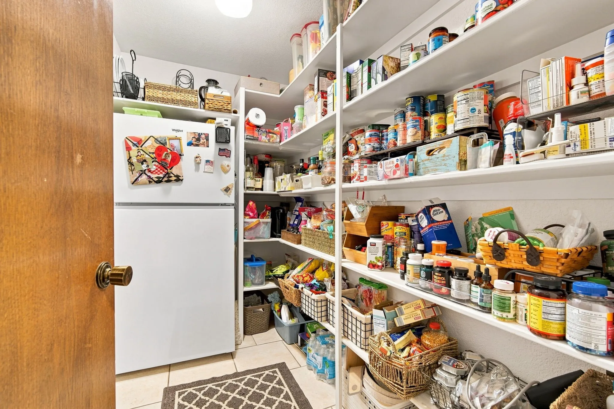 Walk-in pantry featuring extensive built-in shelving, a full-size refrigerator, tiled flooring, and an overhead flush-mount light fixture