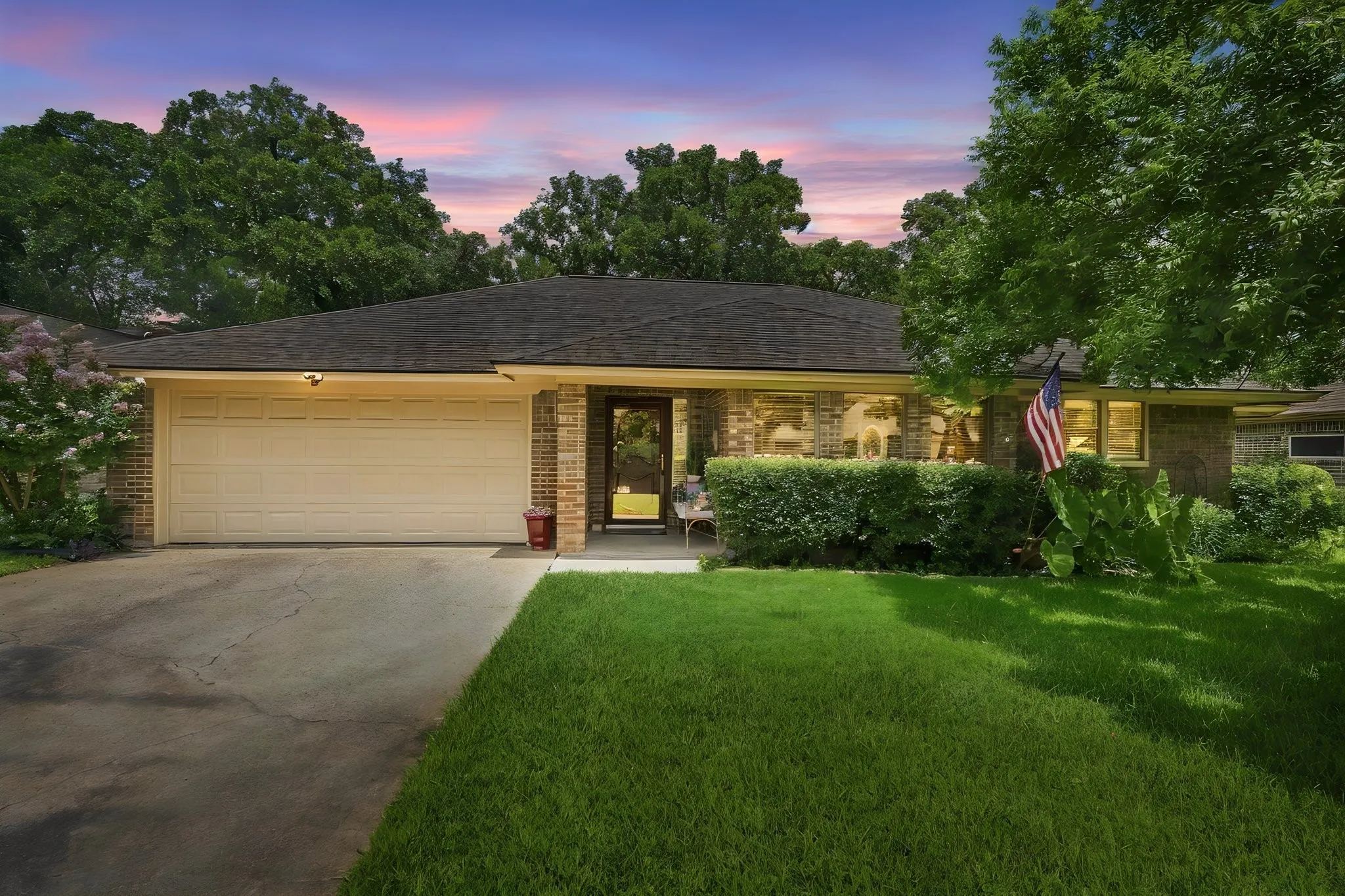 Single-story brick exterior featuring an attached two-car garage, dark shingle roof, and a concrete driveway