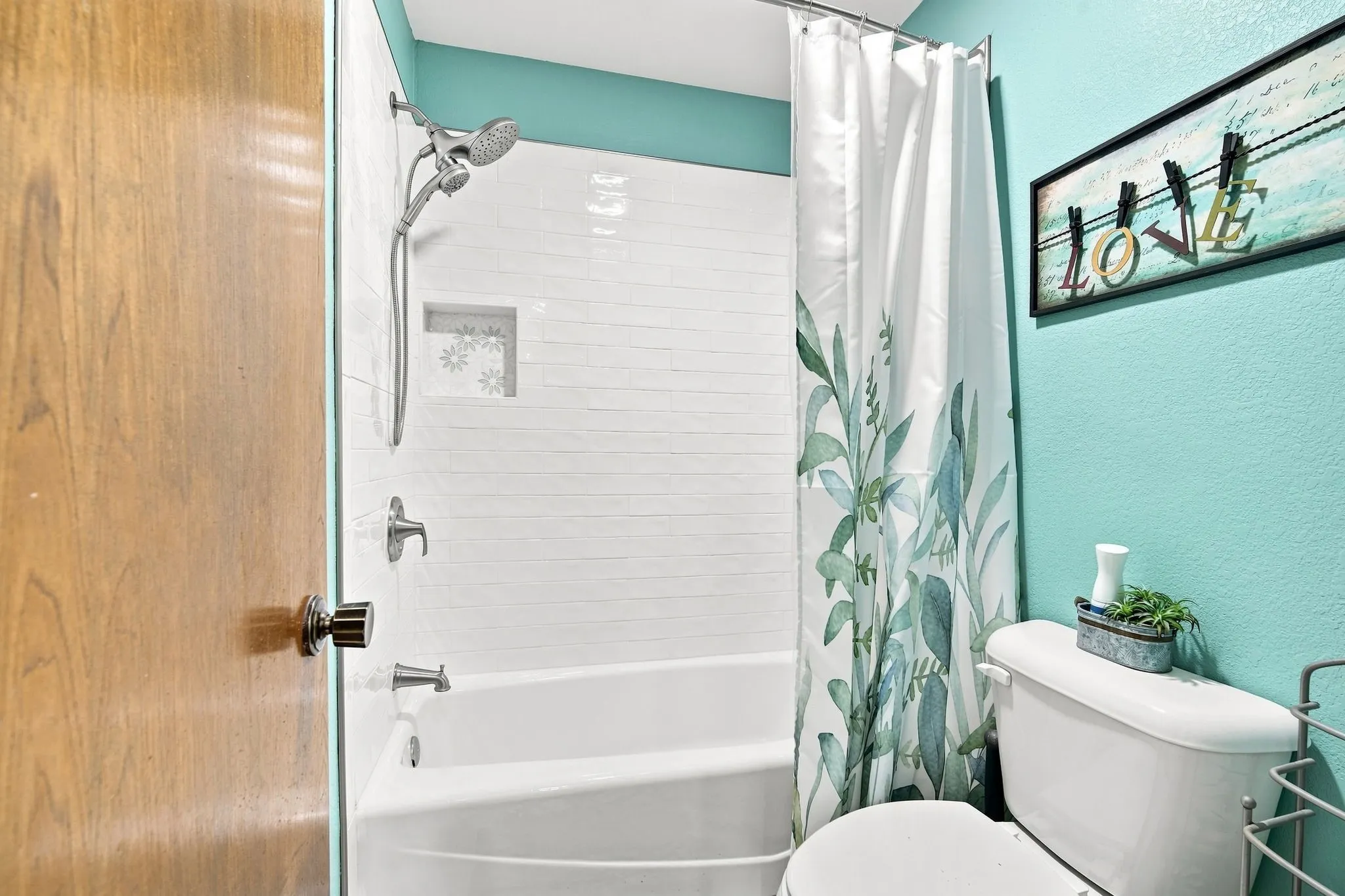 Tub and shower combination featuring white horizontal subway tile surround, recessed shower niche with decorative tile, and a dual-function shower head