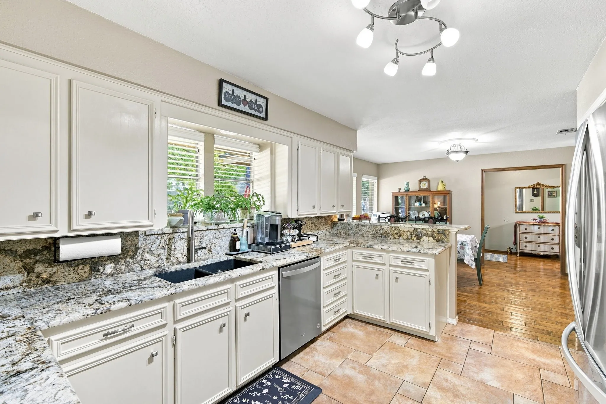 Kitchen featuring a double basin sink, stone countertops, white cabinetry, stainless steel dishwasher, and tile flooring