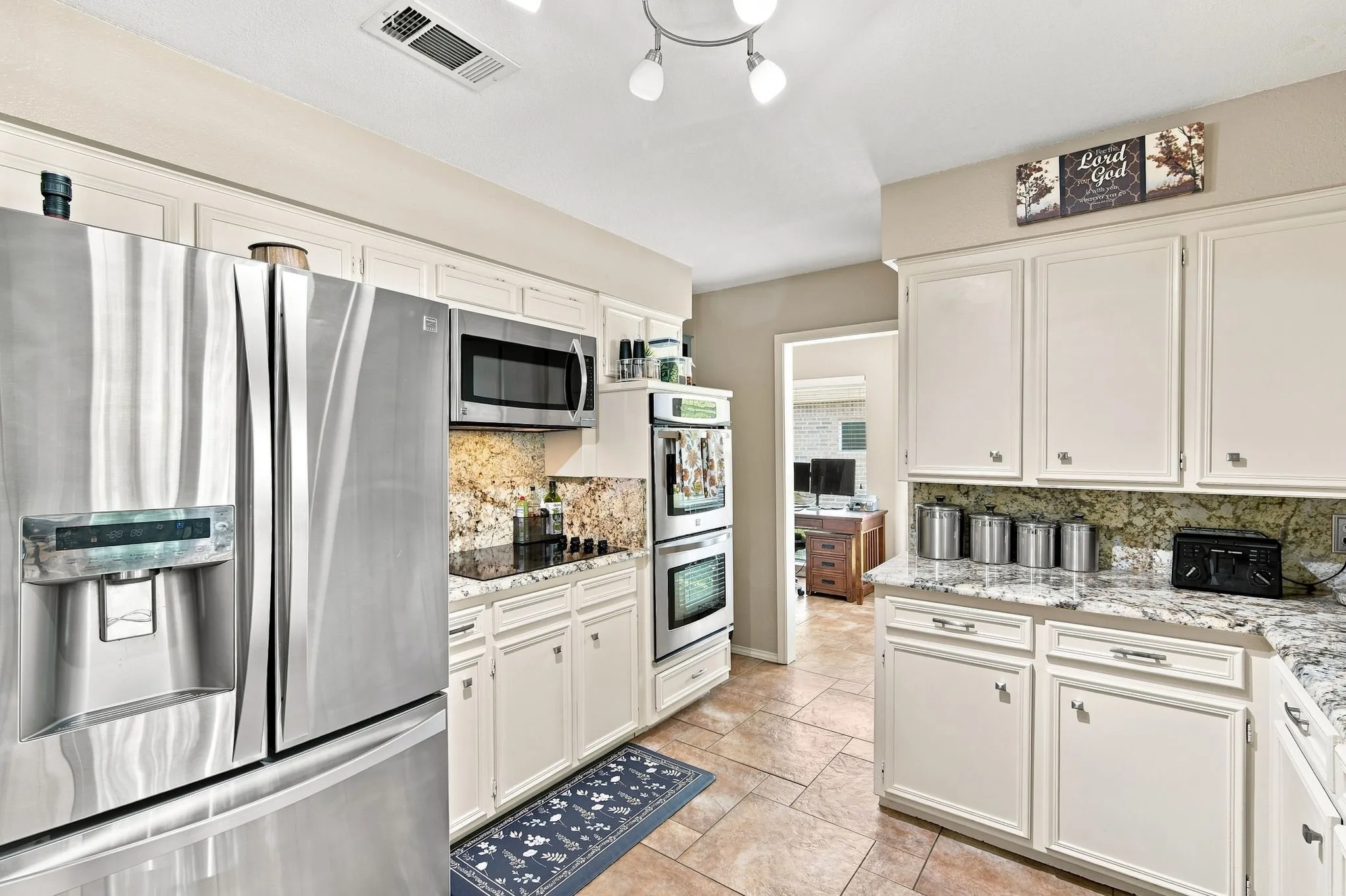 Kitchen featuring extensive white cabinetry, granite countertops, tile backsplash, and stainless steel appliances including a built-in microwave, double wall oven, and refrigerator