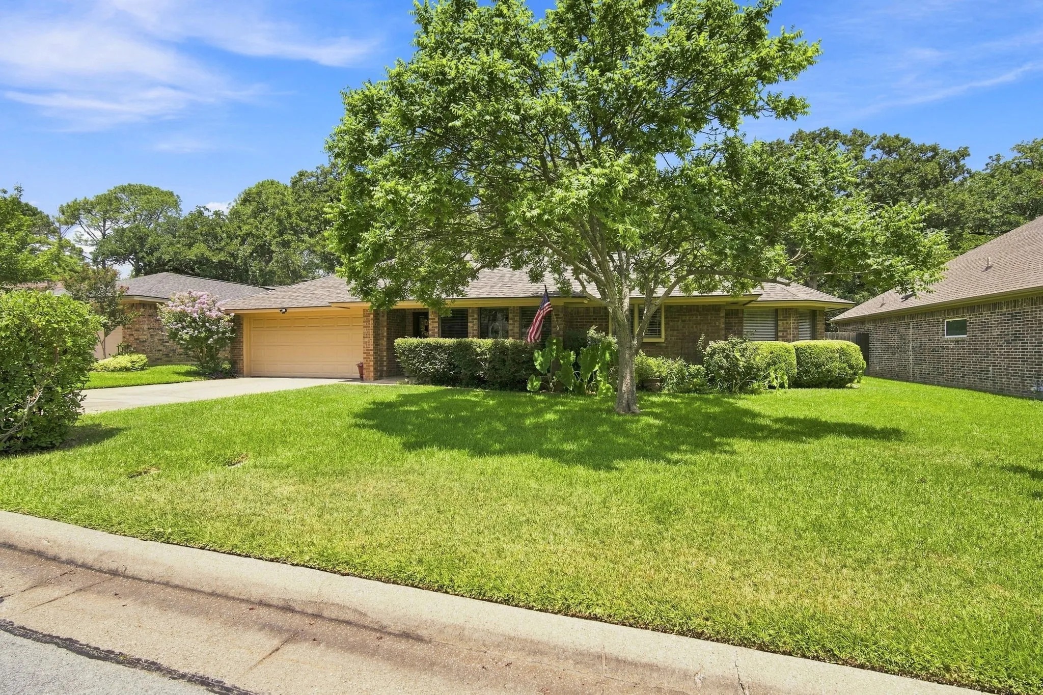 Brick exterior with an attached garage, featuring a concrete driveway and a mature front yard tree