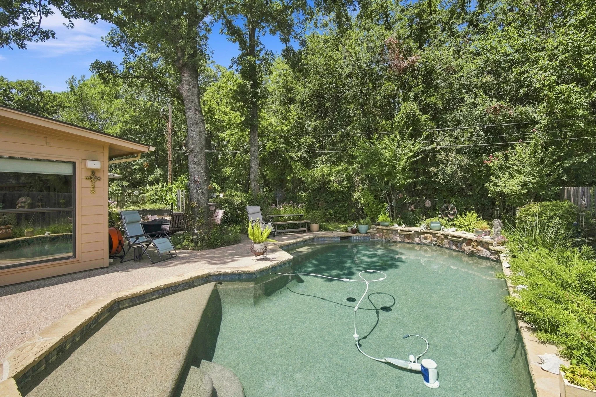 Inviting backyard swimming pool featuring a stone-lined perimeter, integrated water feature, and direct access to a private patio