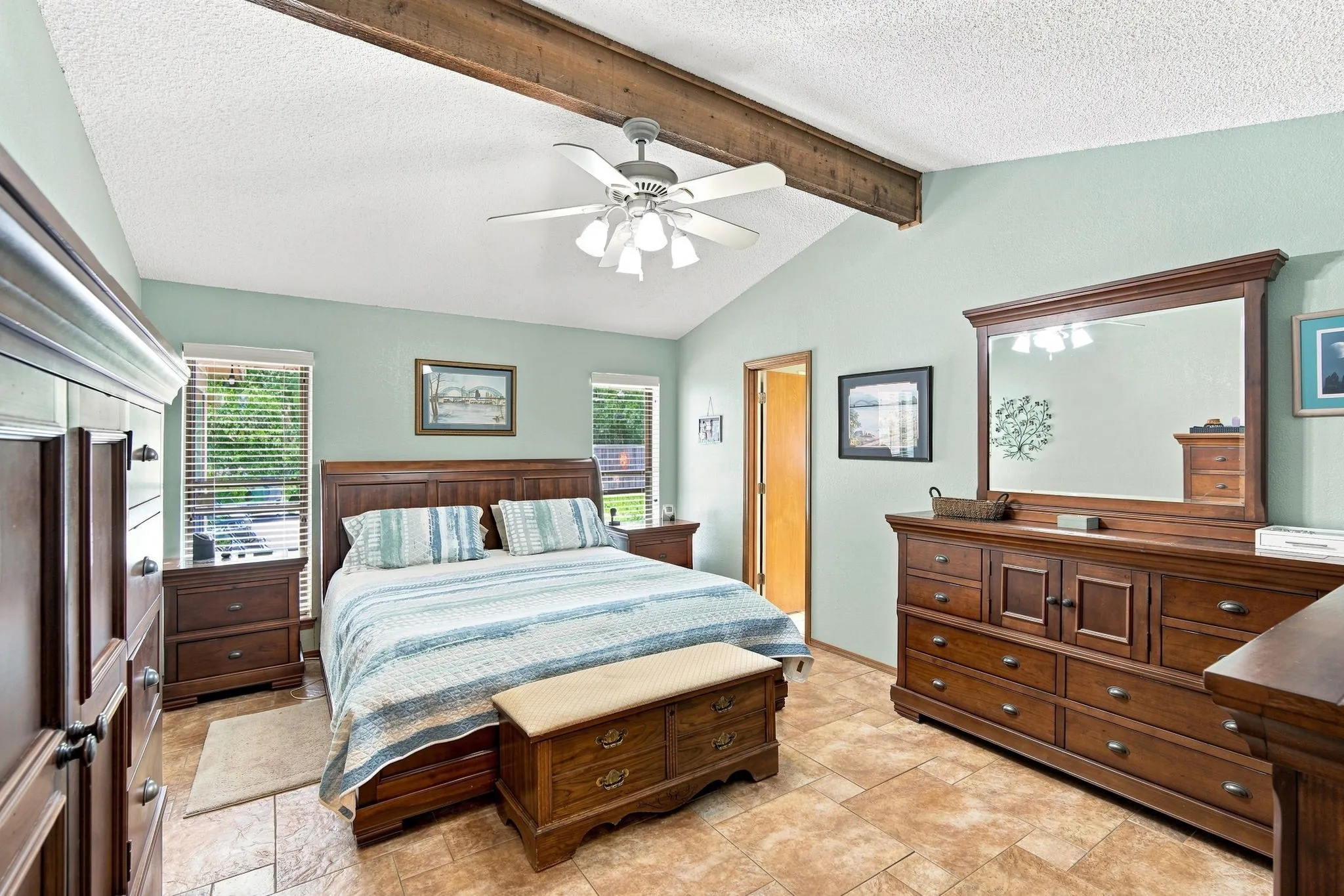 Vaulted ceiling with an exposed wood beam, ceiling fan, and two windows