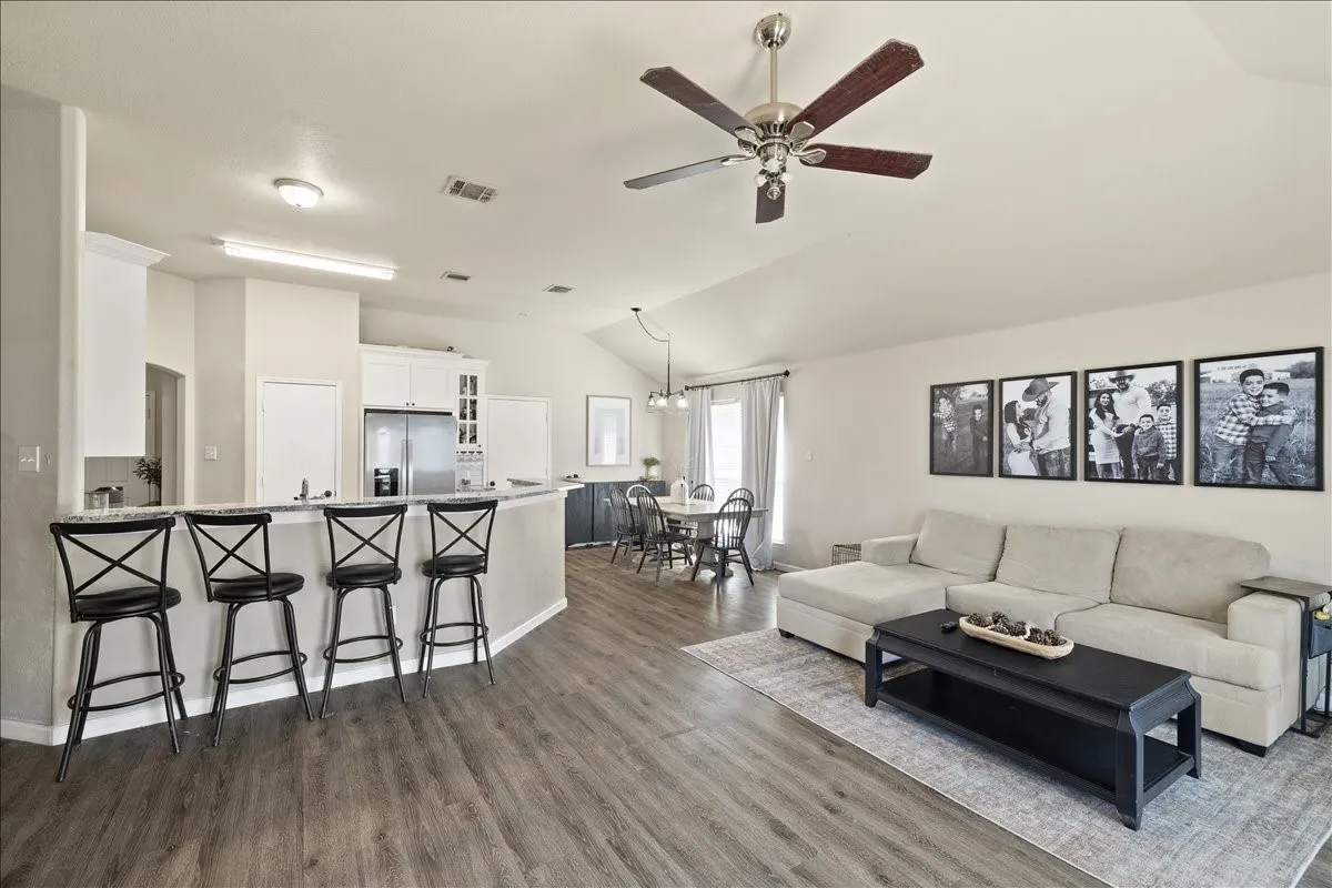 Open-concept living area with wood-finish flooring, vaulted ceiling, and a ceiling fan