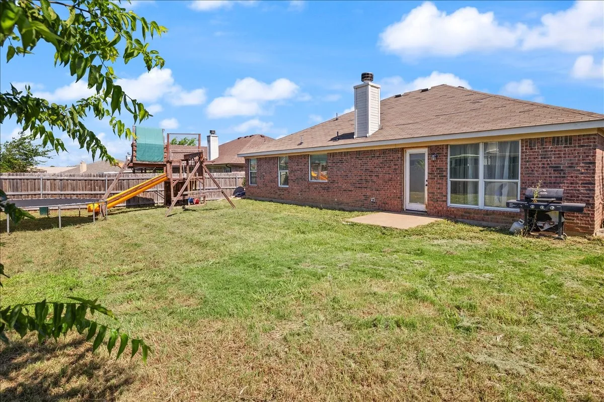 Expansive backyard featuring a red brick exterior, brown shingle roof, white chimney, and a concrete patio