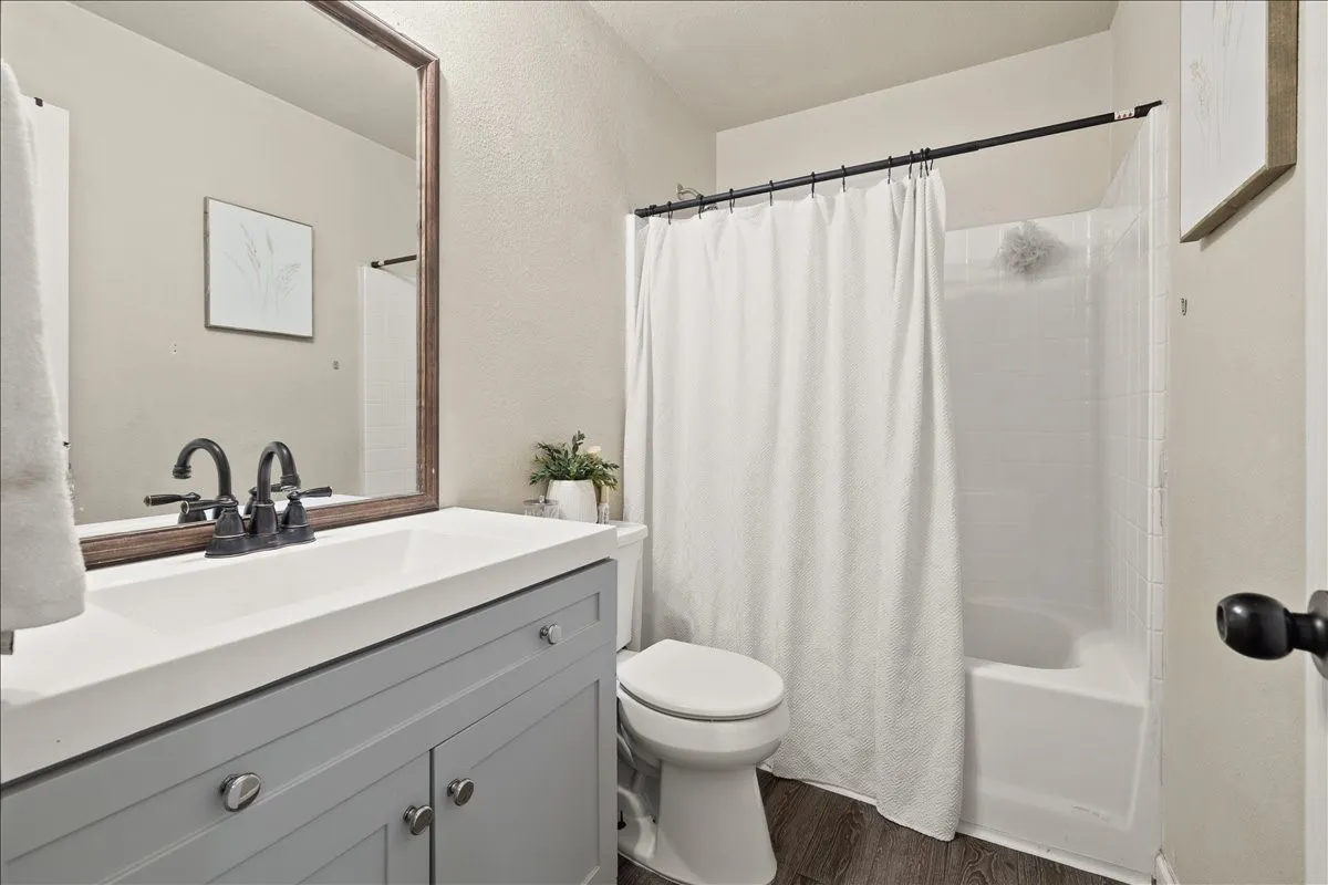 Bathroom featuring a gray vanity with a white countertop, a bronze-framed mirror, and wood-finish flooring