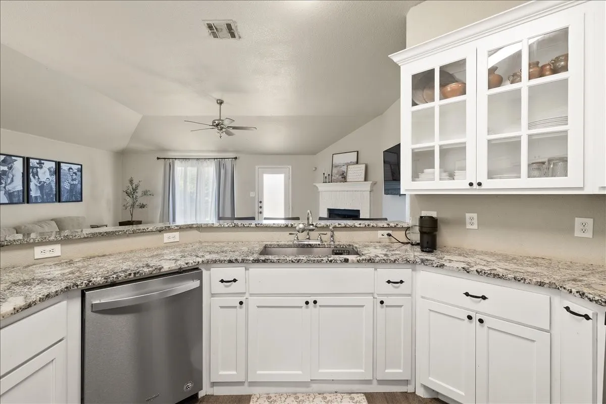 Modern kitchen featuring white cabinetry, stone countertops, a stainless steel dishwasher, and a sink with a gooseneck faucet