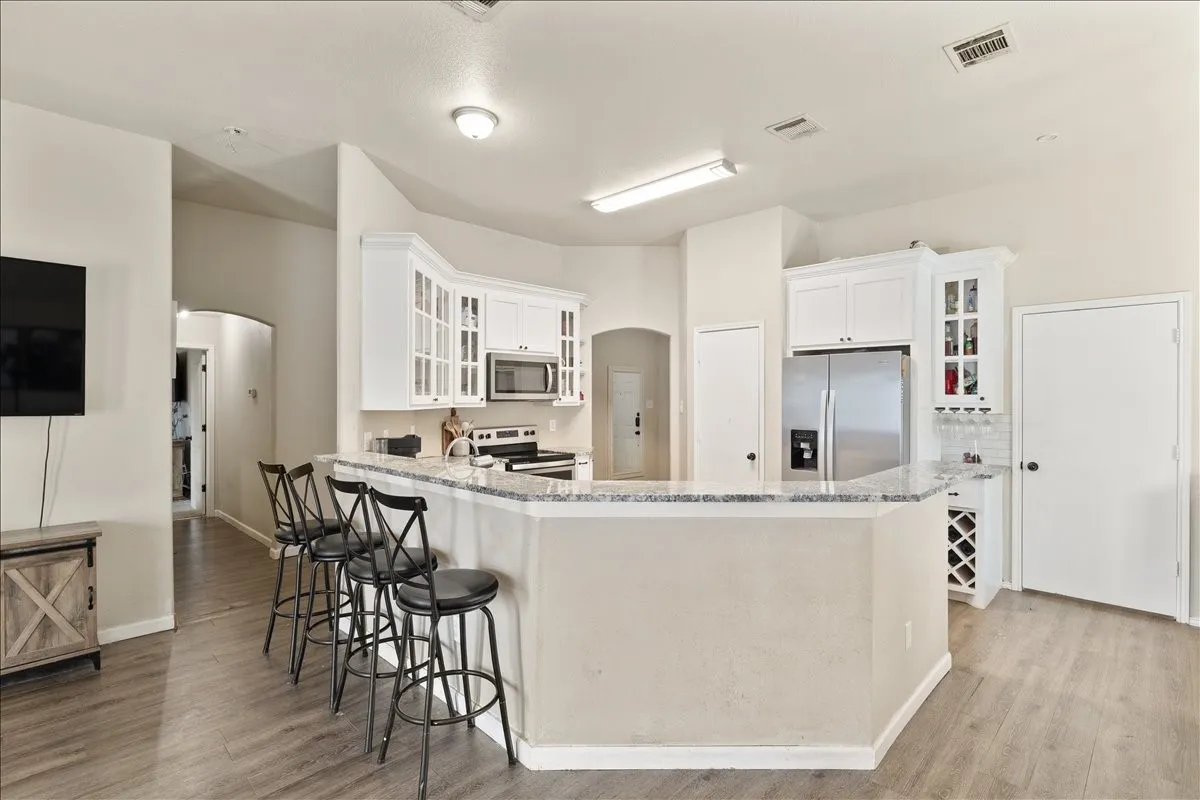 Kitchen featuring a large breakfast bar with granite countertops, white cabinetry, stainless steel appliances, and wood-finish flooring