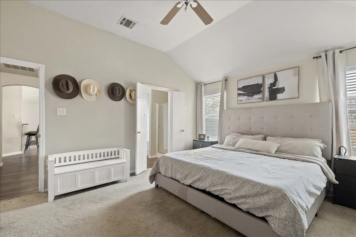 Vaulted ceiling bedroom featuring carpeting, two windows with blinds, and a ceiling fan