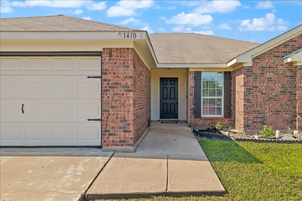 Brick facade home featuring an attached garage with decorative hardware, a covered entry, and a front window with dark shutters