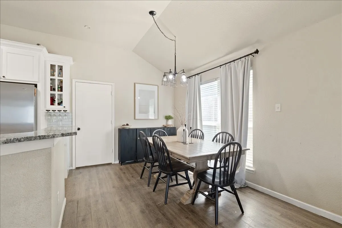 Dining area featuring vaulted ceilings, wood-finish flooring, a contemporary chandelier, and a large window with blinds