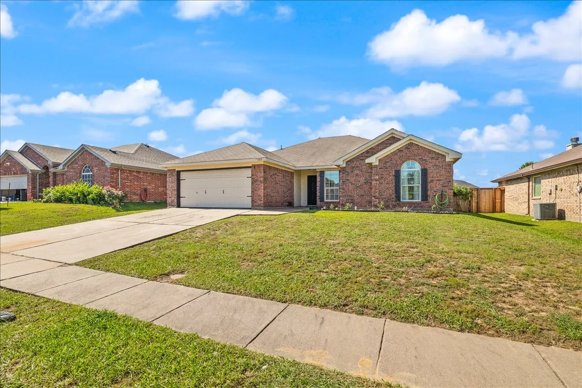 Traditional brick exterior featuring an arched window with shutters, a two-car garage, and a concrete driveway