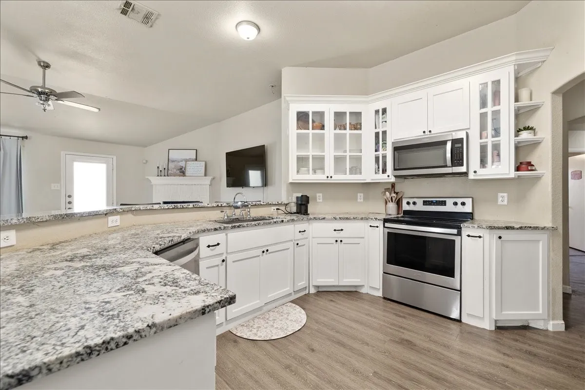Kitchen featuring white cabinetry, granite-finish countertops, stainless steel appliances, and wood-finish flooring