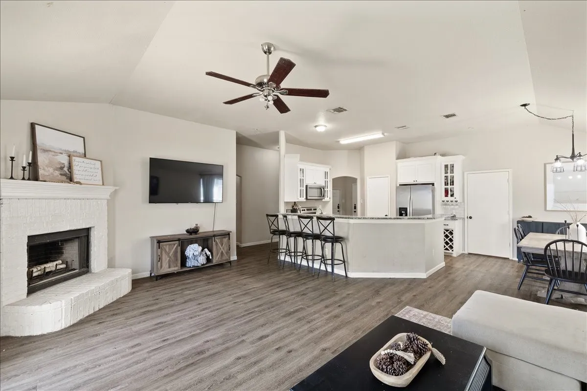 Vaulted ceiling living space featuring a white brick fireplace, wood-finish flooring, and a ceiling fan