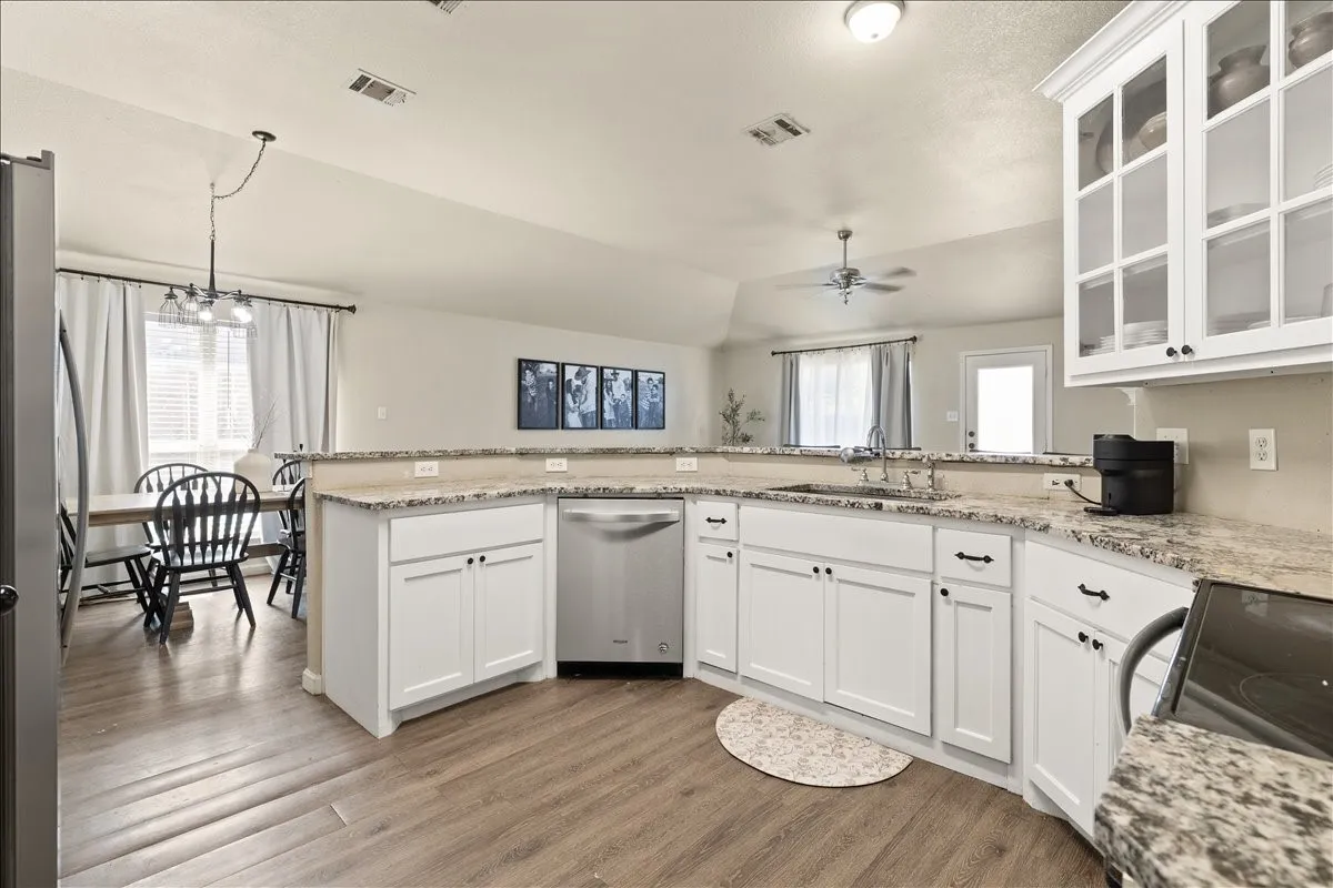 Kitchen featuring white cabinetry, granite-style countertops, stainless steel appliances, and wood-finish flooring