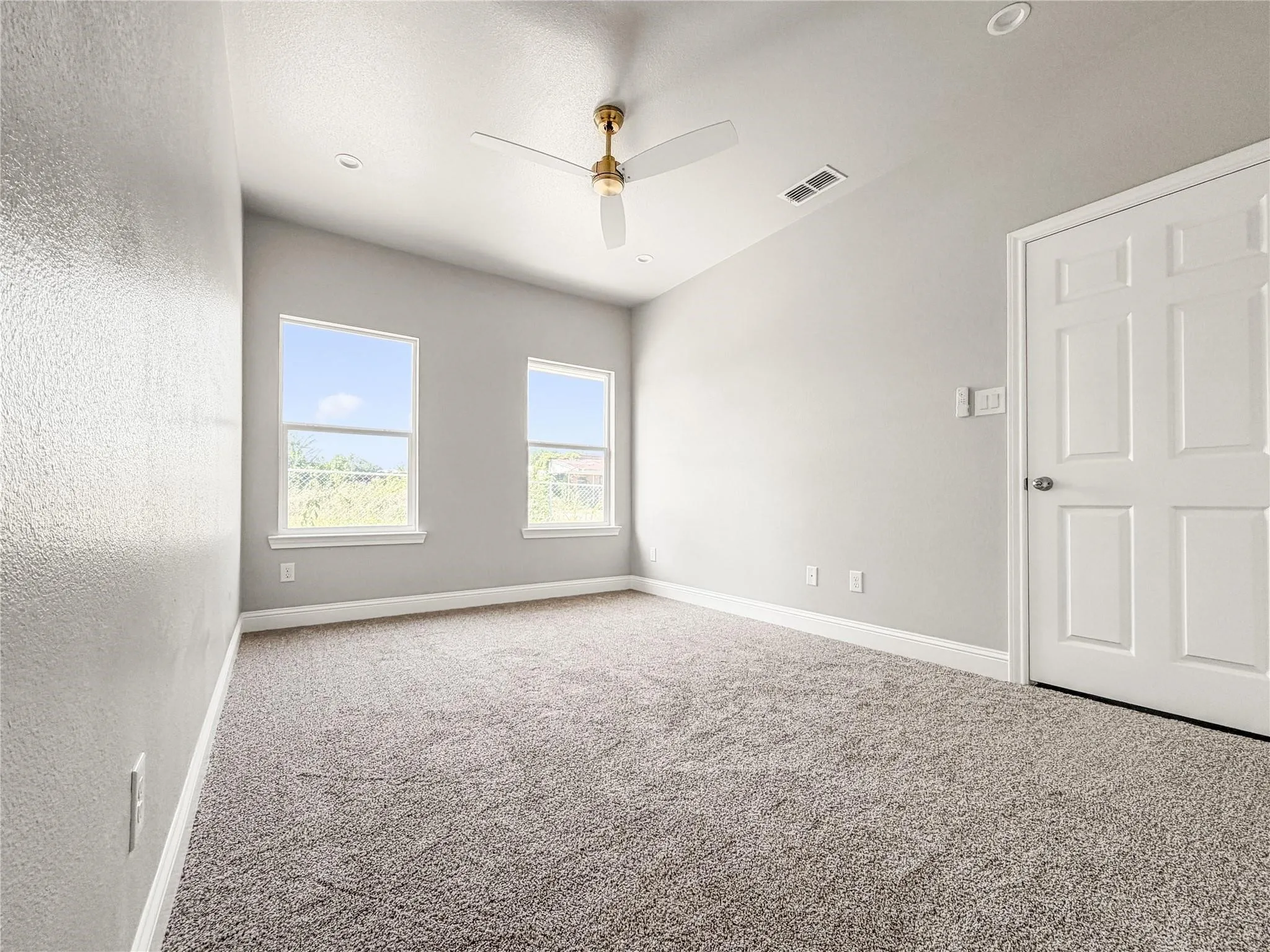 Carpeted interior room with light gray walls, two double-hung windows, a ceiling fan with integrated lighting, and a white six-panel door
