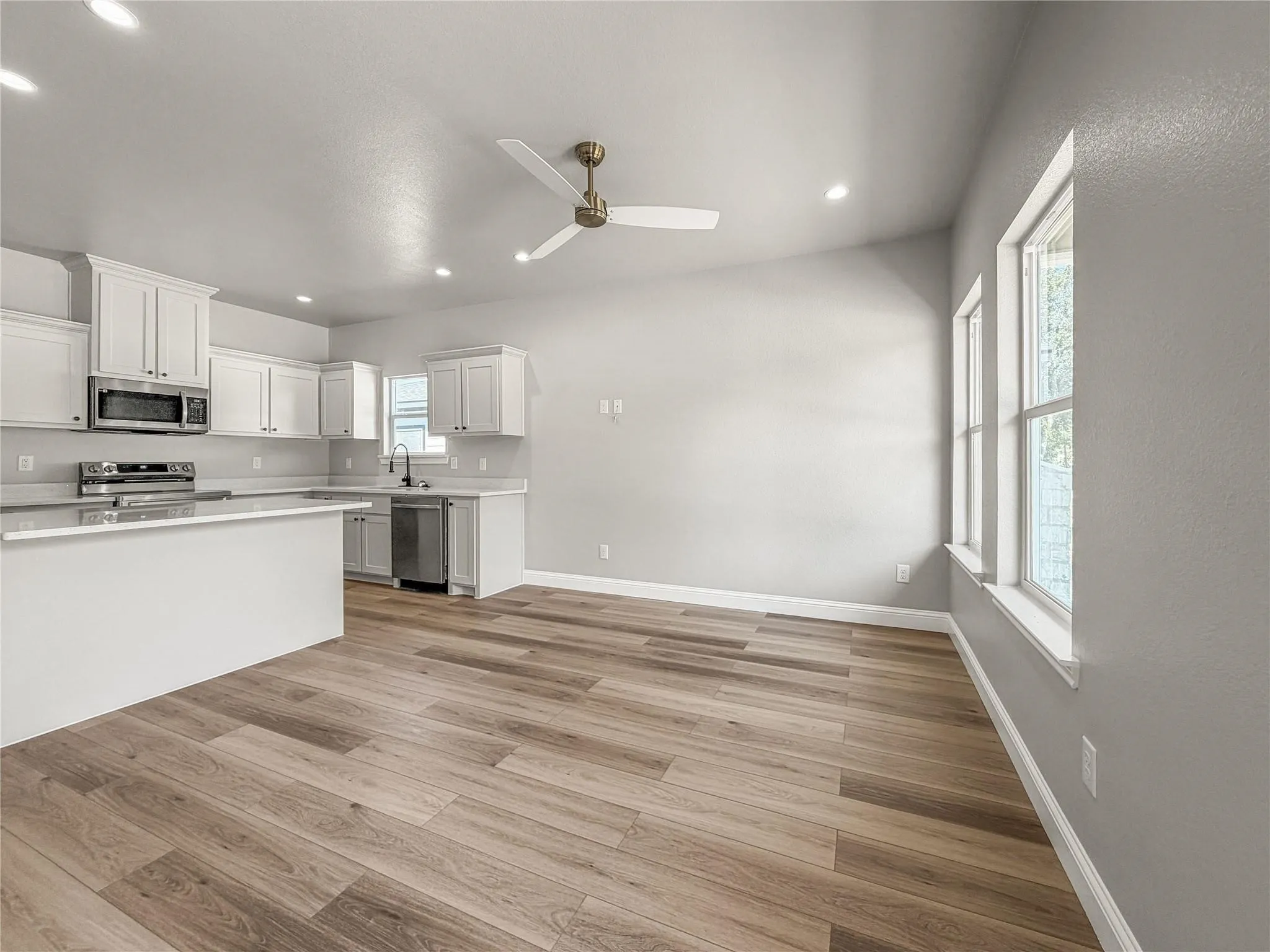 Kitchen featuring white shaker-style cabinetry, light-toned countertops, stainless steel appliances, a black faucet, and wood-finish flooring