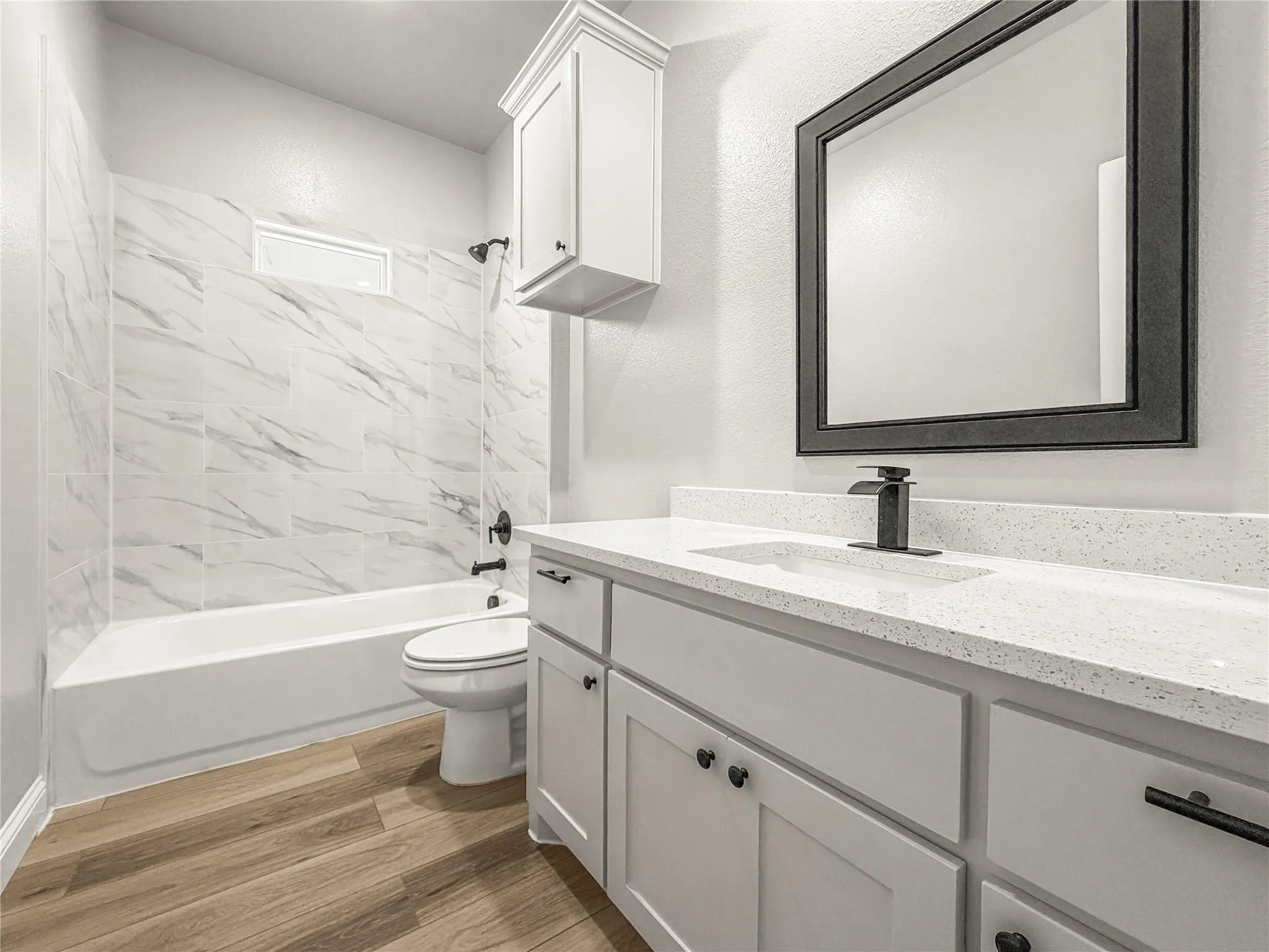 Kitchen featuring a spacious island with a light-toned countertop, wood-finish flooring, white cabinetry with dark hardware, recessed lighting, and stainless steel appliances