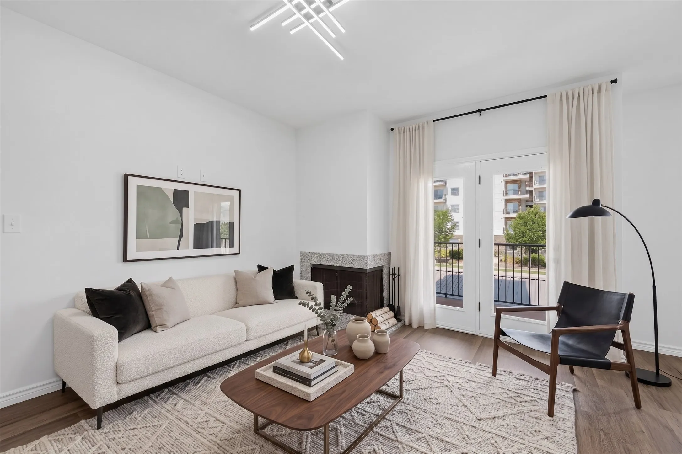 Living area featuring wood-finish flooring, a contemporary fireplace with a stone surround, and double doors opening to a balcony with black railings